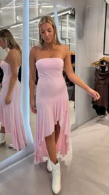 Vestido largo rosado con brillo, strapless y diseño asimétrico con volados en la parte inferior.