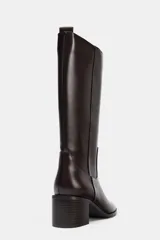Bota alta de caña media en color marrón oscuro, con diseño minimalista, punta redonda y tacón bloque de madera. Cuenta con tirador trasero para facilitar el calce.
