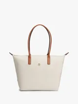 Cartera tote Tommy Hilfiger de nailon color beige, con dos asas superiores de cuero sintético tostado y cierre de cremallera. Presenta el monograma metálico TH en la parte delantera.