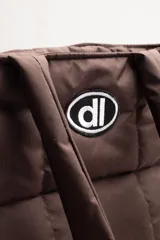 Bolso tipo shopper acolchado color negro, con diseño de cuadrícula. Posee dos asas de hombro y un parche ovalado con un logo estilizado en el frente.