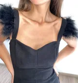 Vestido corto de terciopelo negro, con escote corazón y breteles anchos decorados con plumas negras en los hombros.