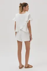 Blusa blanca de lino de manga corta, con volados en las mangas y espalda cruzada adornada con volados.