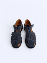 Sandalias cangrejeras de gamuza color marrón, con punta redonda, taco bajo, talonera cerrada y tira con hebilla metálica ajustable en el tobillo.