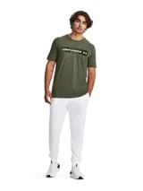 Remera Under Armour de manga corta color verde militar, con cuello redondo acanalado y estampa frontal horizontal con patrón camuflado, el texto "Under Armour" y el logo de la marca.