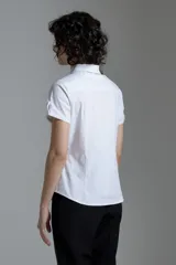 Camisa blanca de corte clásico, con cuello camisero, mangas cortas y cierre frontal con botones.