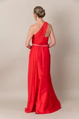 Vestido largo de fiesta color rojo, de corte recto y un hombro descubierto. Presenta una pieza de gasa que nace del hombro, formando el bretel y cayendo a lo largo del vestido.