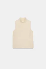 Chaleco de punto color beige, con cuello subido y manga sisa.