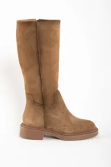 Bota de caña alta color camel, confeccionada en gamuza. Presenta una suela de goma gruesa y plana, y un diseño liso sin cierres visibles.