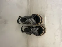 Sandalias negras de cuero con plataforma de madera y suela de goma. Tiras de cuero cruzadas sobre el empeine y ajuste con hebilla al tobillo.