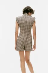 Mono corto de cuello subido y manga sisa con hombreras, con diseño de cuadros tipo tartán en tonos beige y negro. Cuenta con trabillas en los hombros y cierre en la espalda con cremallera oculta.