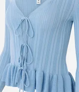 Saco de tricot celeste con textura acanalada vertical, escote en V y cierre frontal con lazos atables. Presenta mangas largas con puños acampanados con volados, al igual que el ruedo.