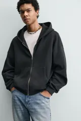 Sudadera tipo hoodie de corte relajado, confeccionada en tejido de algodón con textura estructurada y efecto lavado. Presenta cierre frontal con cremallera, cuello con capucha, manga larga, bolsillos tipo canguro y acabados en rib.