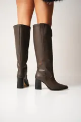 Botas de cuero color marrón con caña alta, punta fina y taco cuadrado.