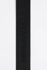 Correa bandolera ajustable de tejido negro con el logo de Bimba y Lola en jacquard. Tiene detalles en piel vacuna negra y herrajes metálicos dorados.