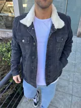 Chaqueta de jean color negro con interior y cuello de corderito sintético blanco. Presenta cierre frontal con botones metálicos y bolsillos frontales con solapa.