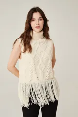 Chaleco de punto sin mangas con cuello polera, diseño de trenzas y rombos en relieve, y detalle de flecos largos en el ruedo.