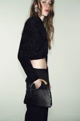 Bolso de mano negro con textura de cocodrilo en relieve, doble asa metálica dorada y cadena bandolera extraíble. Cuenta con cierre de cremallera y bolsillo interior con cremallera.