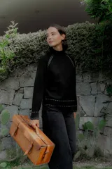 Buzo de punto color negro con cuello alto y detalles de pespuntes decorativos en color blanco en las costuras de las mangas, puños y ruedo.