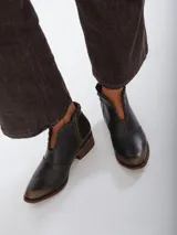 Botinetas de cuero color marrón con efecto desgastado en la puntera y el talón. Presentan un diseño con corte en V en el empeine con detalles de costuras decorativas, cierre lateral y taco bajo de madera.