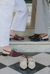 Sueco de cuero color borgoña con cordones, ojales y hebillas plateadas. Tiene tira trasera regulable con elástico.