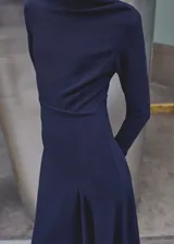 Vestido midi de color azul marino con diseño evasé, cuello barco y manga larga. Presenta cintura fruncida, bajo asimétrico y cierre de cremallera en la parte posterior.