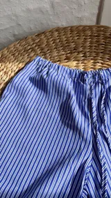 Pantalón palazzo celeste a rayas verticales blancas, de tiro alto y corte holgado.