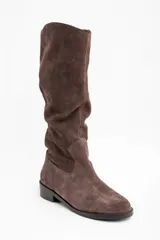 Bota de caña alta confeccionada en gamuza color marrón, con diseño de caña holgada y suela plana con pequeño taco cuadrado.