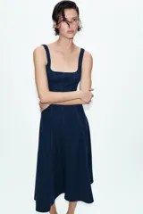 Vestido midi de color beige con escote cuadrado y tirantes anchos. Presenta un diseño entallado en el torso con costuras verticales marcadas y una falda con caída evasé.