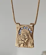 Collar dorado con dije rectangular con imagen religiosa y cristales azules.