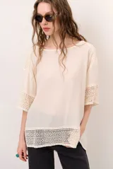 Blusa color blanco, de corte holgado y mangas tres cuartos, con detalles de encaje y bordados en las mangas y en el ruedo.