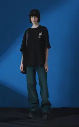 Remera de manga corta y cuello redondo con calce oversize. Presenta una estampa frontal en color crema con diseño artístico de un ángel y una rosa, acompañada de frases en español. Confeccionada en algodón premium.