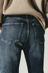 Jeans de tiro alto color marrón oscuro con acabado lavado, corte recto/flare y bajo cropped sin costuras. Presenta cinco bolsillos y cierre frontal con cremallera y botón metálico.