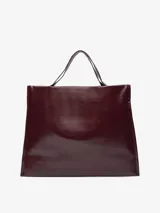 Maxi shopper de diseño minimalista con acabado brillante y textura craquelada. Cuenta con un compartimento principal con cierre magnético, bolsillo interior con cremallera y asas de hombro integradas. Logo de la marca grabado en la parte inferior frontal.
