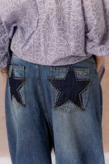 Jean wide leg de tiro alto y lavado azul desgastado, con cinco bolsillos y detalles de estrellas en denim oscuro con tachas metálicas en los bolsillos traseros.