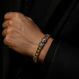 Pulsera de eslabones tipo cubana en acero con baño de oro, destacada por un cierre central con diseño de flor de lis en tono plateado.