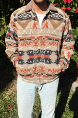 Campera beige con estampado azteca en tonos marrón, naranja y azul marino. Tiene cuello de corderito color beige, cierre con botones a presión, dos bolsillos laterales y puños con botón.