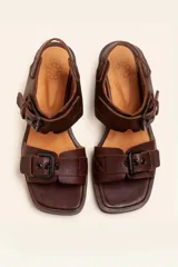 Sandalias de cuero negro con taco bloque de madera tallada, tiras con hebillas grandes y punta cuadrada.