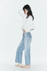 Jeans de tiro bajo con corte wide leg y largo cropped. Presenta diseño de cinco bolsillos, trabillas para cinturón y cierre frontal con cremallera y botón metálico.