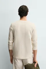 Camiseta de manga larga en tejido de estructura canalé, con cuello redondo y cierre frontal de botonadura. Presenta un corte relajado y puños acanalados.