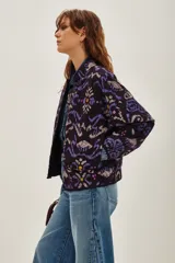 Campera bomber acolchada con estampado geométrico en tonos violeta, azul y negro. Presenta cierre frontal con botones a presión, cuello redondo y puños elásticos.