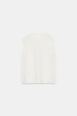 Camisa blanca sin mangas, con cuello redondo y detalle de encaje y bordados florales en el frente.