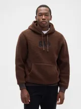 Buzo tipo canguro de textura teddy, color marrón, con capucha ajustable mediante cordones, bolsillo frontal tipo canguro y logo de la marca bordado en el pecho.
