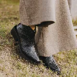 Bota corta de cuero vacuno con acabado metalizado y textura de reptil. Presenta punta fina, cierre lateral interno y taco cuadrado de madera.