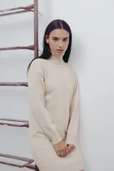 Vestido corto de tejido de punto en color beige, con cuello alto y mangas largas. Presenta puños y ruedo acanalados, con un diseño de calce relajado.