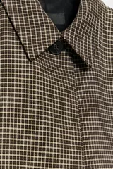 Blazer corta de corte recto con estampado de cuadros pequeños en tonos marrones y negros. Presenta cuello solapa, manga larga y cierre frontal con un botón.