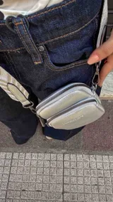 Bandolera compacta color rojo con textura de cuero, correa regulable y desmontable con diseño de rayas rojas y blancas. Cuenta con bolsillos frontales y cierre, interior forrado en tela.