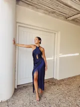 Vestido largo azul con escote halter cruzado, abertura en el pecho, falda drapeada con flecos y corte irregular.