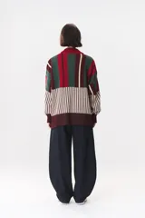 Buzo oversize de tejido de punto con diseño de bloques y rayas verticales en colores rojo, verde, bordó y crema. Presenta cuello alto tejido y terminaciones en rib en puños y ruedo.