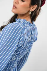 Vestido largo a rayas verticales azules y blancas, con manga globo y diseño de nido de abeja con hilo elástico hasta la cintura. Cuello alto fruncido y falda amplia con caída fluida.