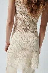 Vestido corto de crochet color beige, sin mangas, con escote redondo y diseño ligeramente acampanado en el bajo.